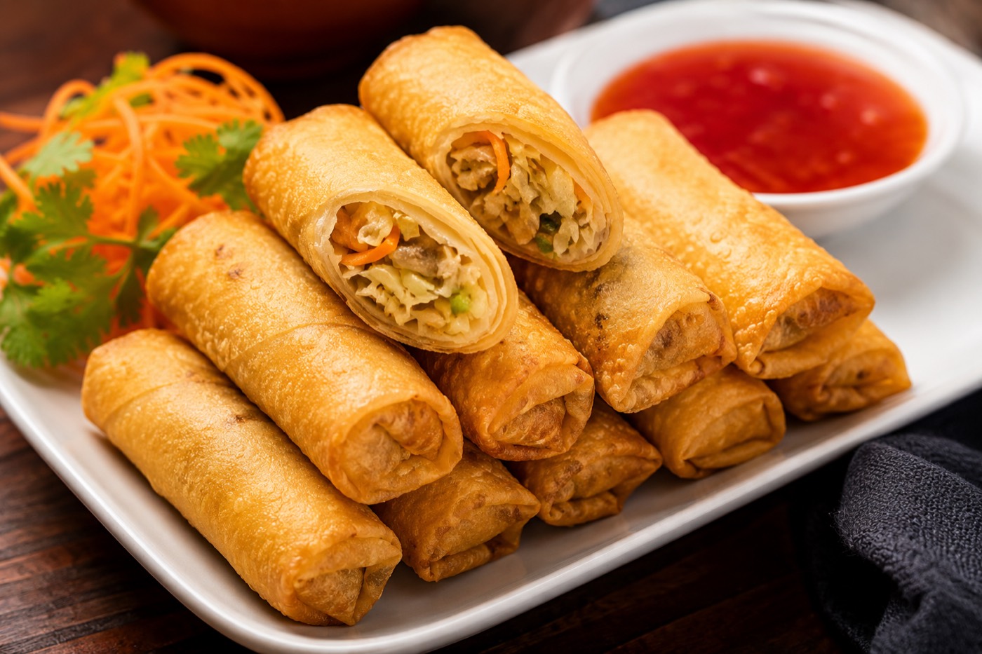 Golden fried egg rolls stacked on a plate with sweet chili dipping sauce